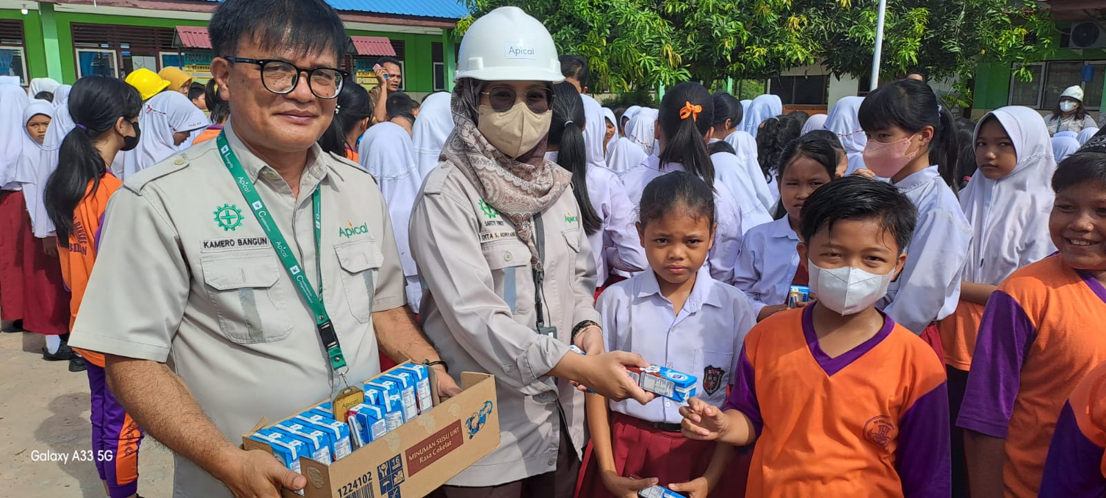 Foto Kamero Bangun Humas Apical membagikan susu kepada murid sekolah.